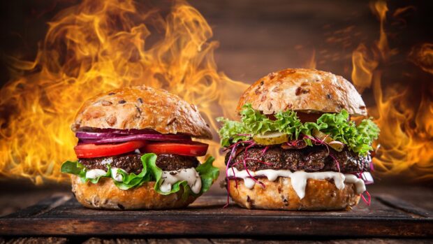 Two delicious hamburger burgers with lettuce and tomato against a fiery background