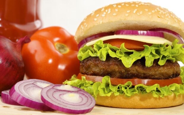 Close up view of hamburger with fresh lettuce tomato and onion slices on a wooden surface