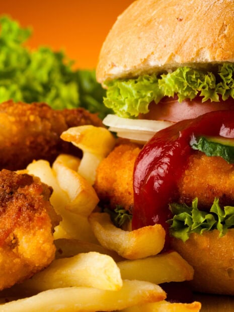 A close up of a crispy chicken sandwich with lettuce tomato and fries on an orange background