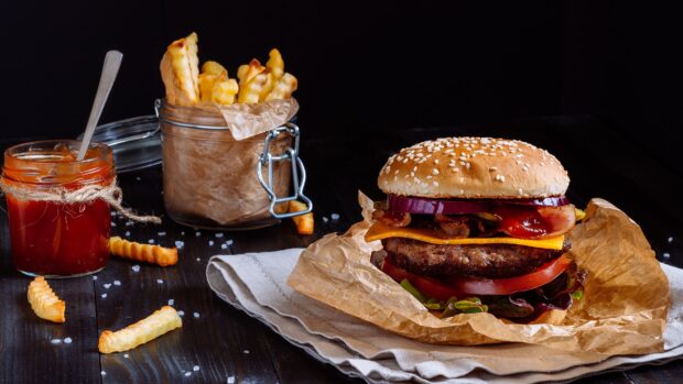 A delicious hamburger with cheese bacon and fresh vegetables on a wooden table with crispy fries and ketchup sauce