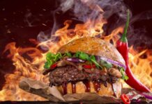 A delicious hamburger with lettuce bacon and chili pepper on a smoky background with flames
