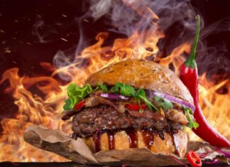 A delicious hamburger with lettuce bacon and chili pepper on a smoky background with flames