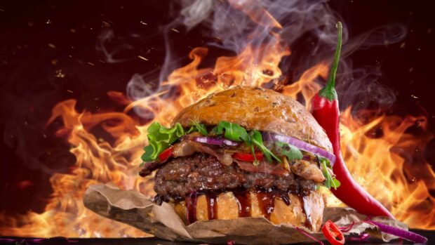 A delicious hamburger with lettuce bacon and chili pepper on a smoky background with flames