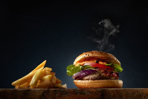 A delicious hamburger with lettuce tomato and onion served with French fries on a wooden surface