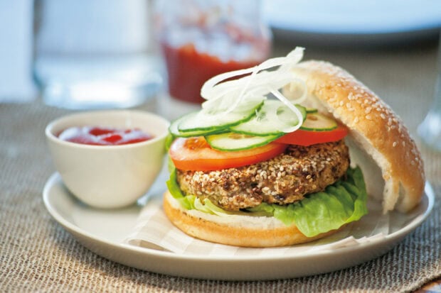 A healthy hamburger with quinoa patty lettuce tomato cucumber and onion slices on a sesame bun