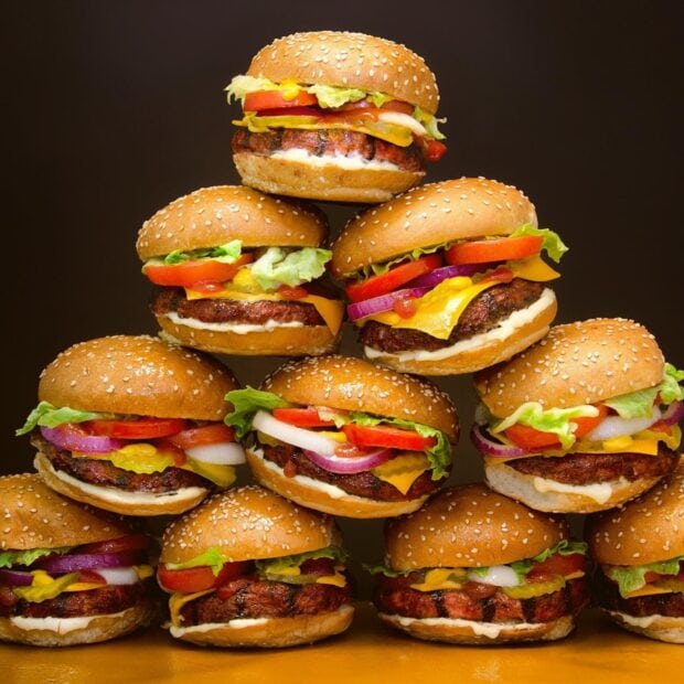 A stack of grilled hamburger with lettuce tomato and cheese on sesame seed buns