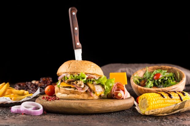 Delicious hamburger with lettuce cheese and bacon on wooden board with side dishes