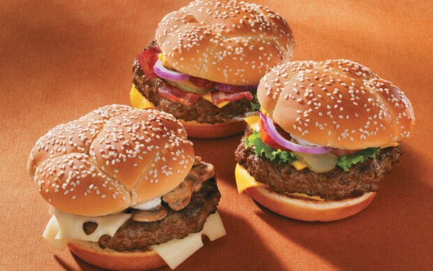 Three different hamburger with sesame seed buns and various toppings on brown surface