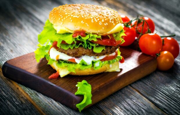 A delicious hamburger with fresh lettuce and sauce on a wooden cutting board