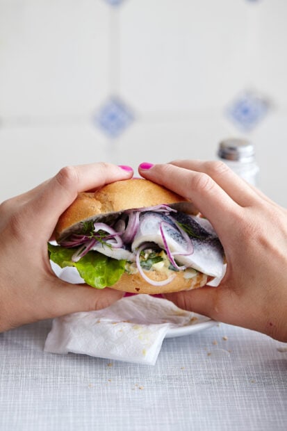 A person holding a fresh hamburger with lettuce and onions filling
