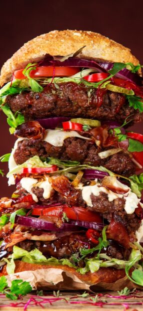 A towering hamburger stacked with fresh lettuce tomato onion and grilled beef patties