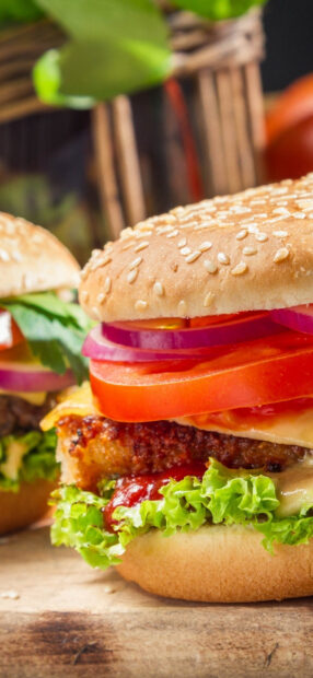 A close up of fresh hamburger with lettuce tomato and onion on a sesame seed bun