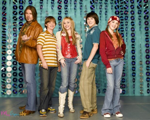 The Hannah Montana cast standing in front of a backdrop with CDs in a group pose