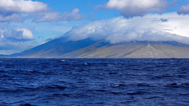 Large Hawaiian Islands mountain landscape seen from the ocean with wind turbines under cloudy sky