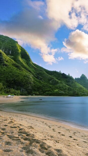 A peaceful beach with sand and green mountains in Hawaiian Islands under a blue sky
