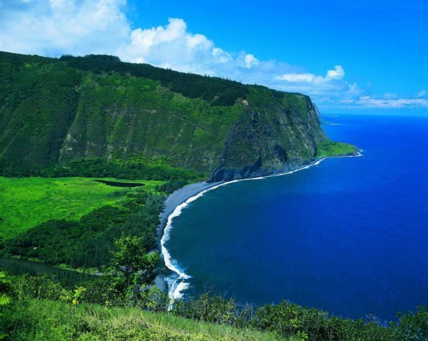 Lush Hawaiian Islands coastline with green cliffs and deep blue ocean under clear sky