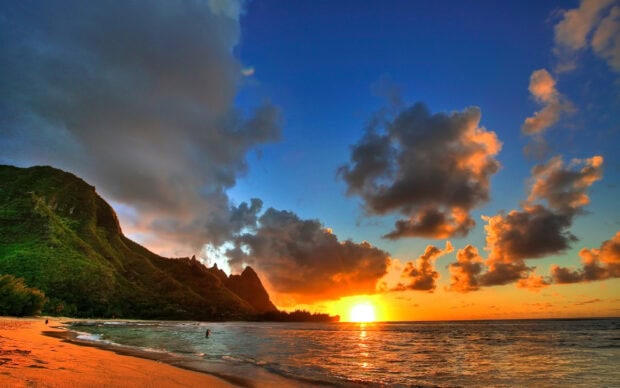 Stunning Hawaiian sunset with ocean waves and lush mountains under vibrant sky