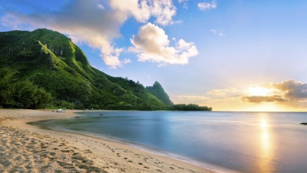 A serene Hawaiian ocean scene with lush green mountains and sandy beach at sunset