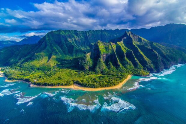 Lush Hawaiian coastline with vibrant green cliffs and turquoise ocean waves under a cloudy sky