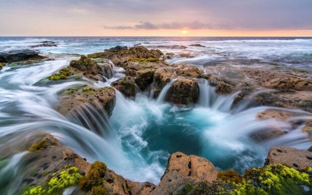 Waves swirl around a volcanic rock formation in the Hawaiian Ocean during sunset