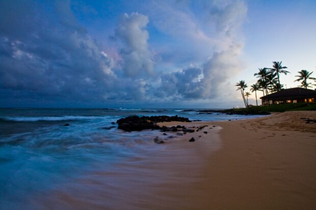 Calm Hawaiian ocean waves gently washing over the sandy shore during twilight