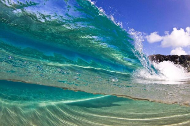 Clear ocean wave under the blue sky in Hawaiian waters with sandy seabed visible