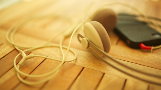 Beige headphones with cable lying on wooden surface next to a smartphone