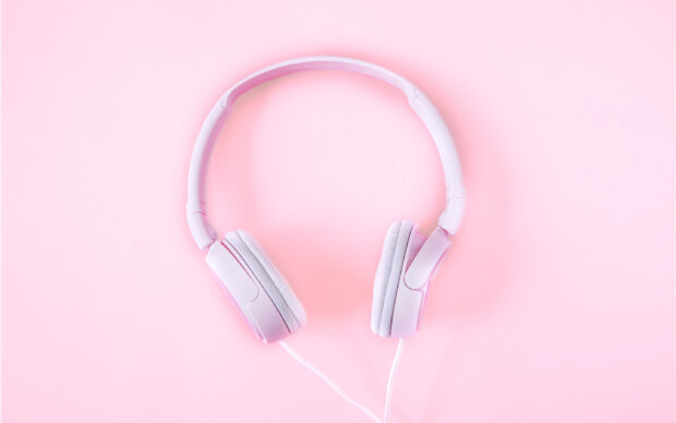Pink headphones resting on a pastel pink surface with a clear cable attached
