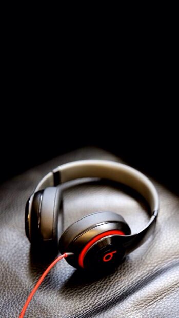 Black headphones with red cable resting on a leather surface