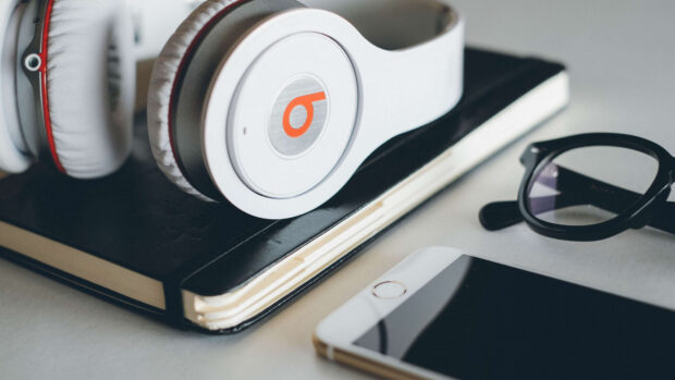 White headphones resting on a notebook with glasses and a smartphone nearby