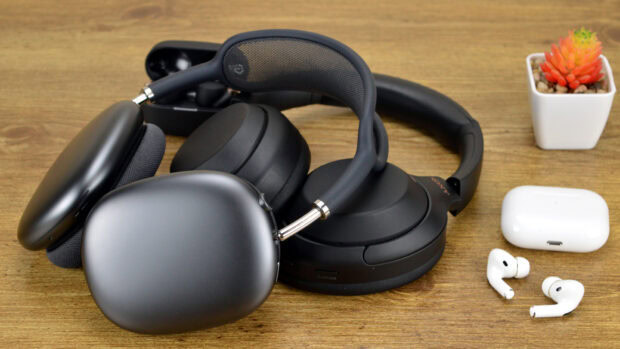 Black headphones and earbuds resting on a wooden surface with a small potted plant nearby