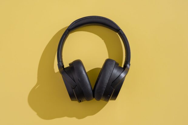 Black headphones resting on a yellow surface casting a shadow