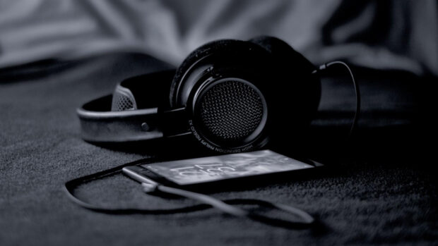 Black headphones resting next to a smartphone on a dark surface with a cable attached