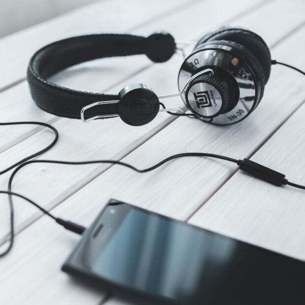 Black headphones placed on a white surface next to a smartphone with a connected cable