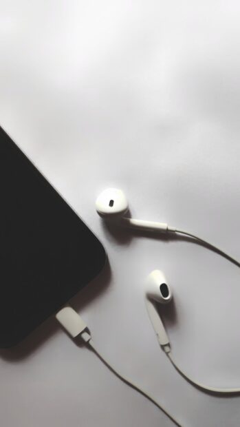White headphones connected to a black phone on a white surface