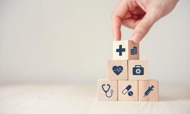 Wooden blocks with health symbols and a hand stacking a medical cross block