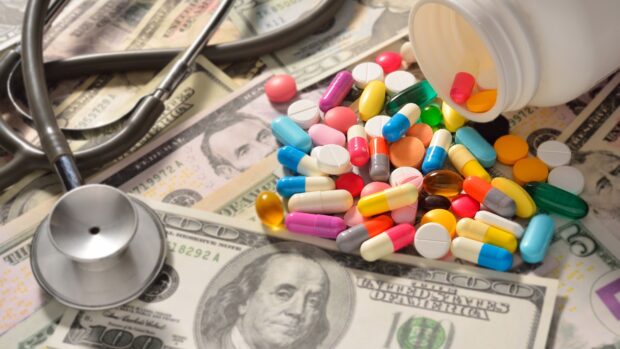 A stethoscope and colorful medicine capsules scattered on US dollar bills illustrating health costs