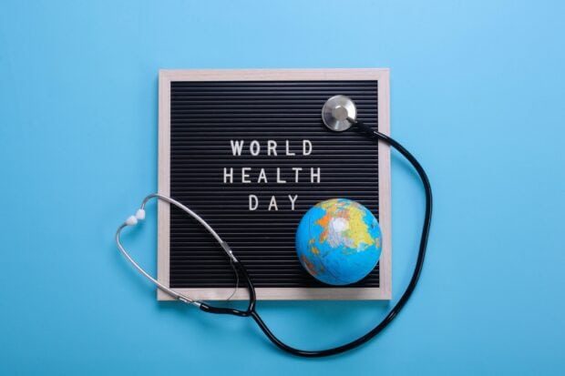 A stethoscope and globe next to a board with the words world health day on a blue surface