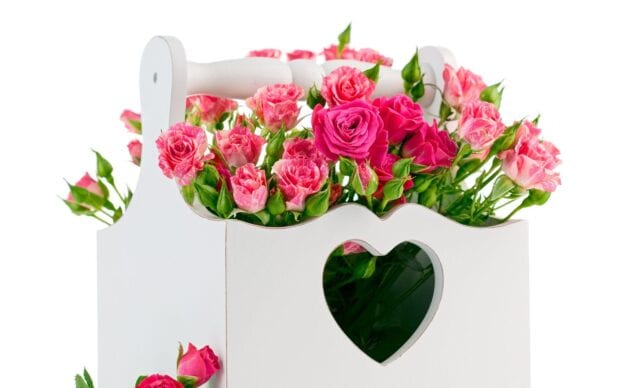 Pink and red roses arranged in a white wooden box with a heart cutout design
