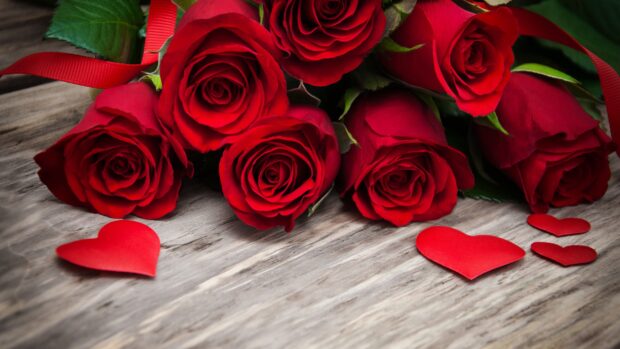A close up of hearts and flowers showing red roses on a wooden surface with decorative red hearts