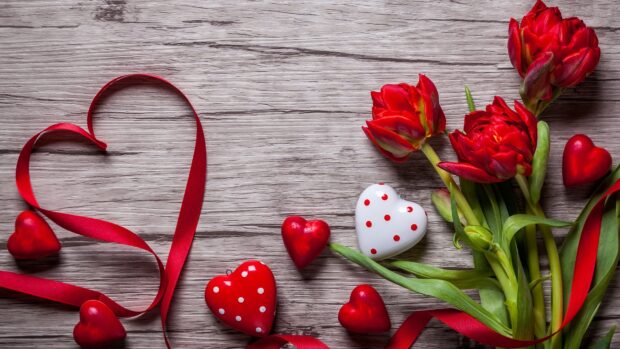 Red ribbon shaped hearts and red tulip flowers on wooden surface with hearts and flowers decoration