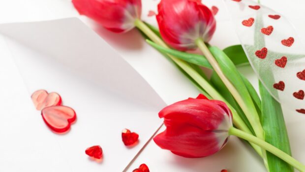 Red tulips with green stems and hearts decoration on a white surface