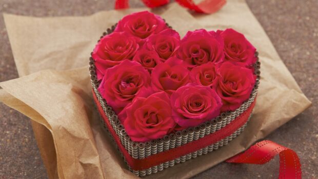 A heart arrangement of roses surrounded by chocolate sticks and ribbon on craft paper