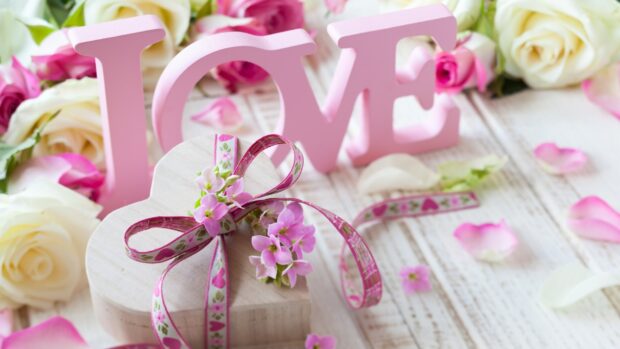A wooden heart decorated with pink flowers and ribbon symbolizing love and hearts