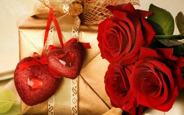 Red hearts with roses and a golden gift box on a table with a leaf