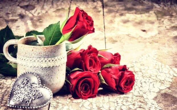 A decorative heart and red roses arranged beside a ceramic mug with green leaves