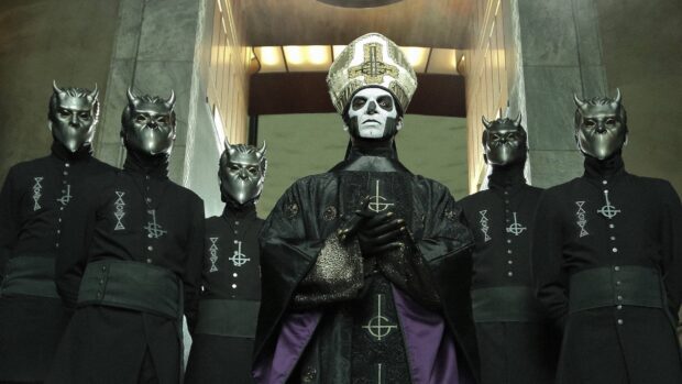 The heavy metal band leader dressed in ceremonial robes with menacing masked band members standing behind
