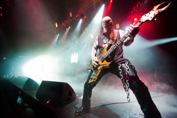 A heavy metal guitarist with chains performs on stage under bright lights