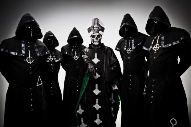 A heavy metal band dressed in dark robes with a skeleton figure wearing a ceremonial outfit in the center