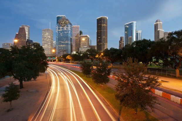 Houston city skyline with illuminated buildings and light trails on highway at dusk